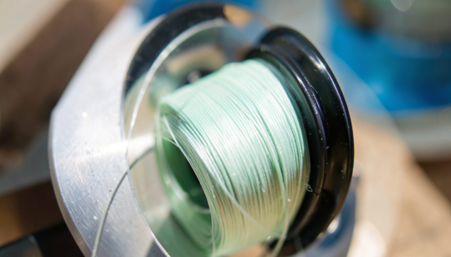 Spool of fresh fishing line being wound onto a reel, bright monofilament catching the light