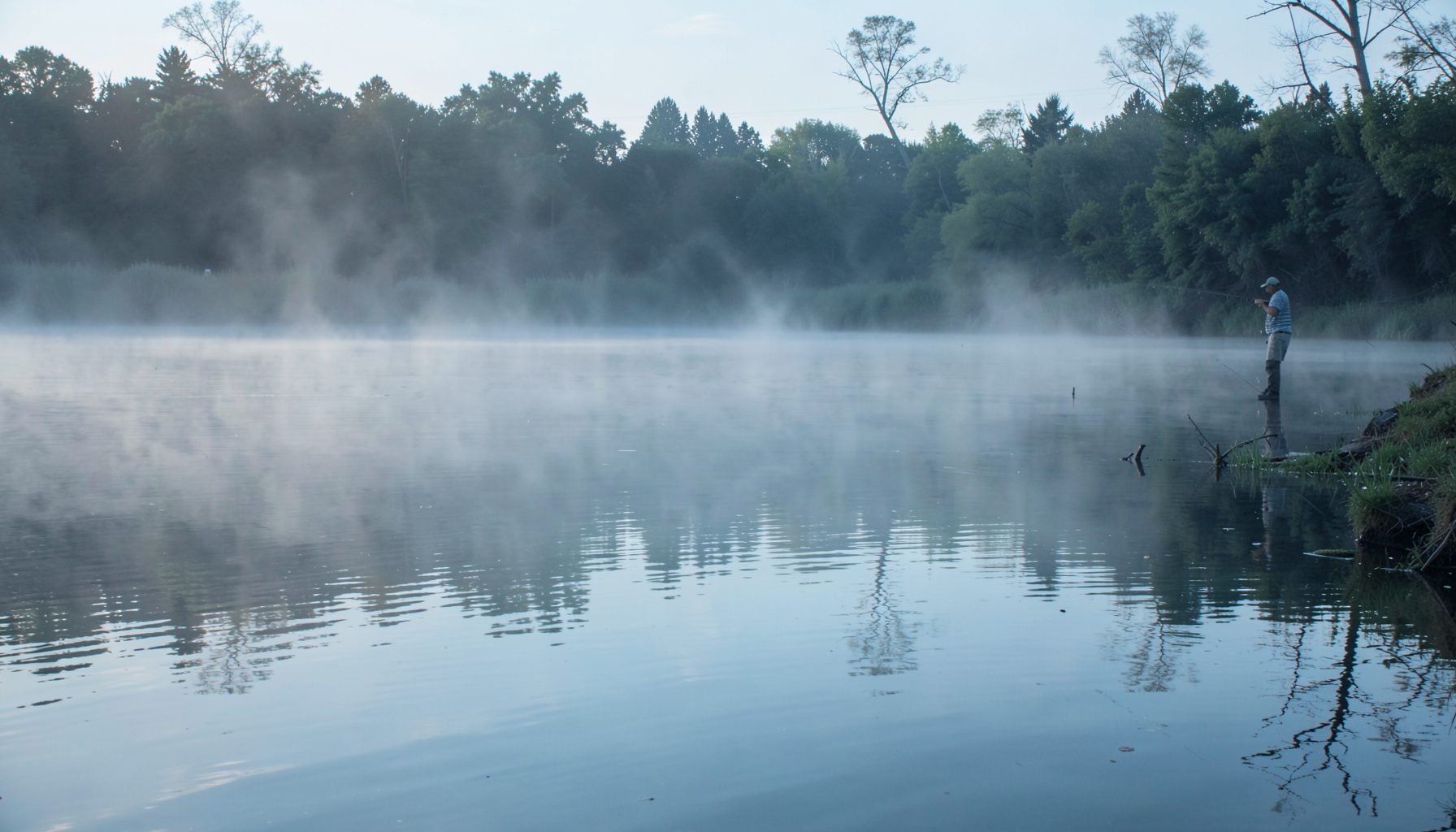 Deep stillwater venue with a pole angler on the far bank, mist rising off the surface